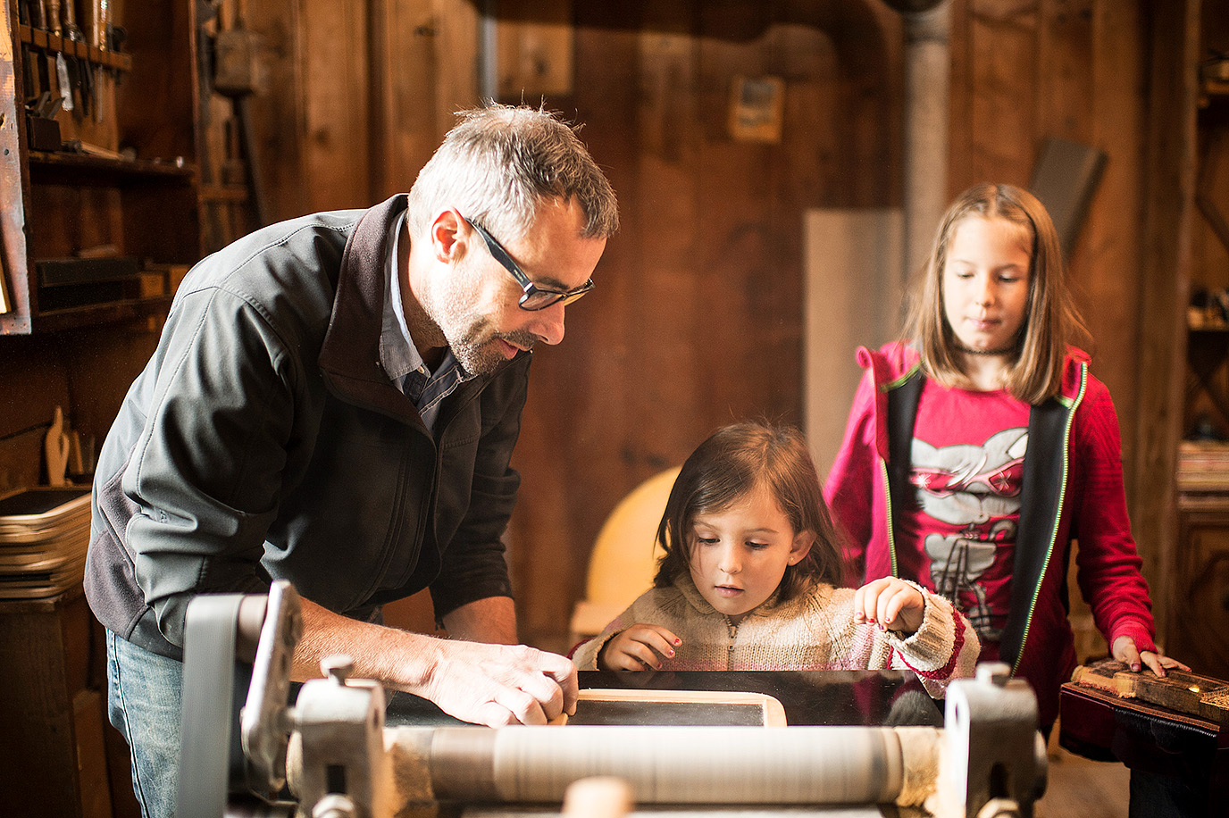 Ein Mann zeigt zwei Mädchen in der Schiefertafelfabrik Elm eine historische Maschine