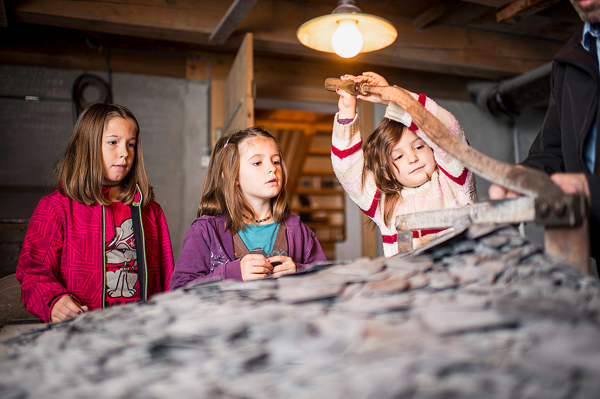 Drei Kinder schauen in der Schiefertafelfabrik Elm zu, wie Schiefer bearbeitet wird