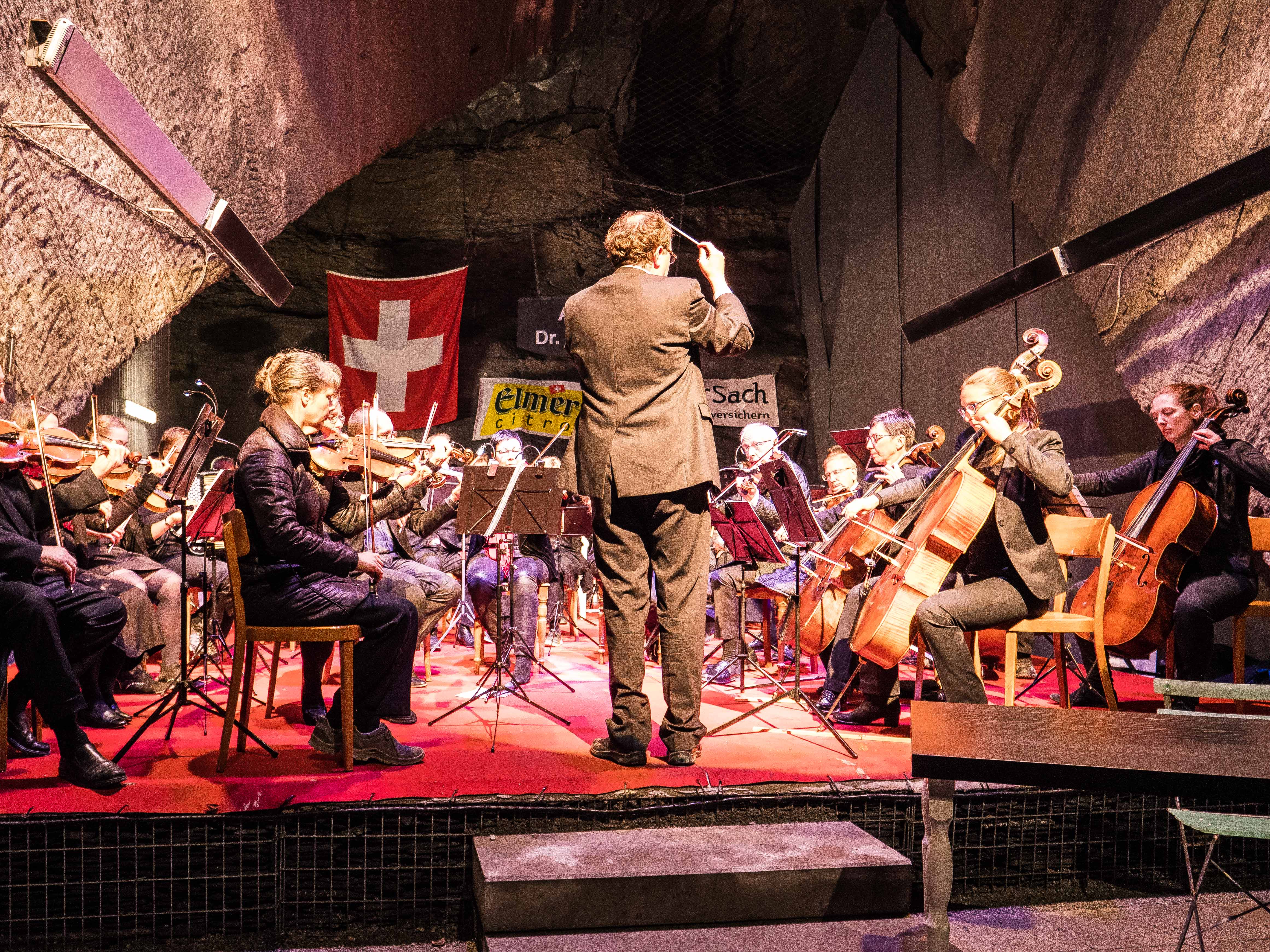 Streicher und Dirigent vor einer Schweizer Fahne im Auditorium