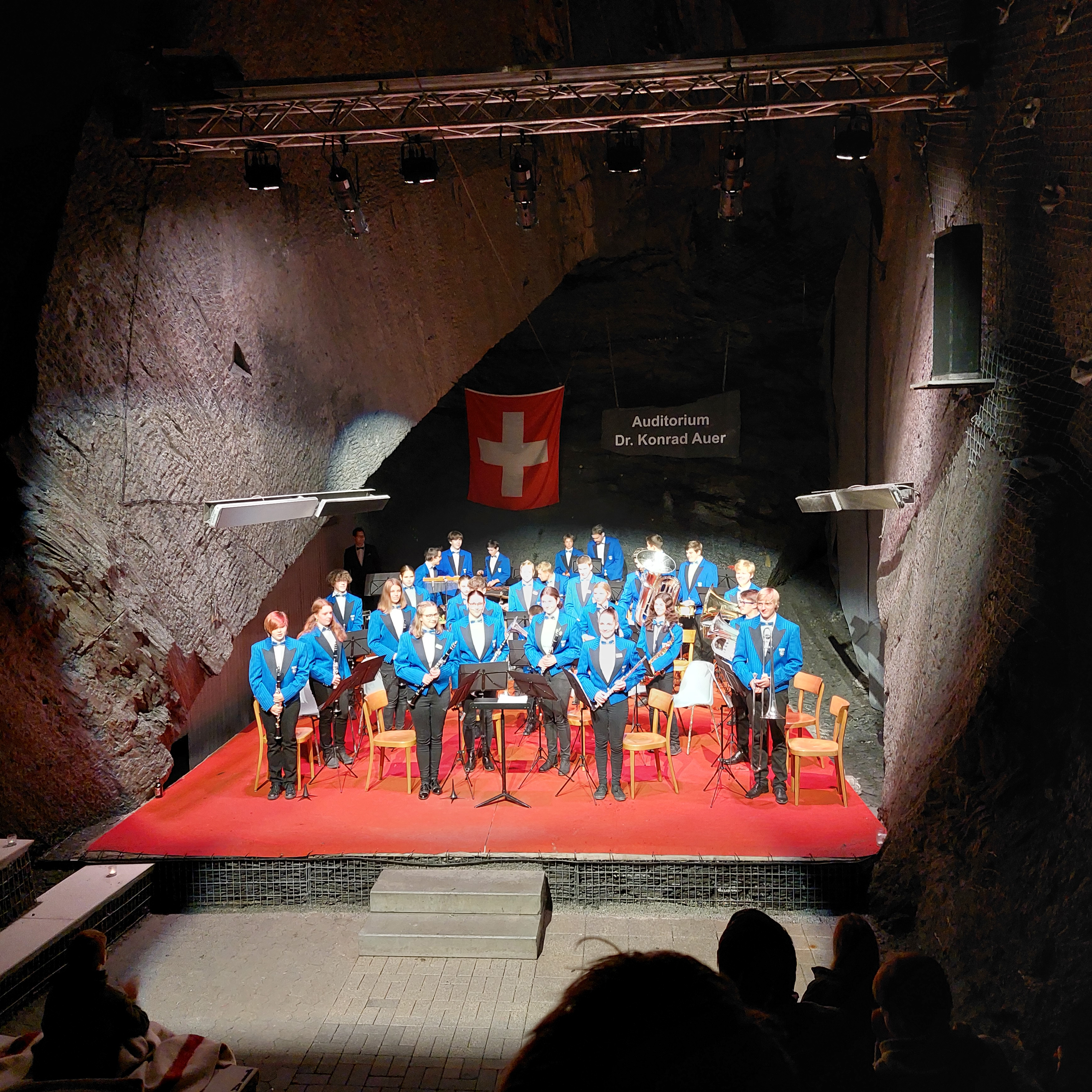 Jugendliche Blasmusikerinnen und -musiker in blauen Jacken auf der Bühne im Auditorium des Landesplattenbergs
